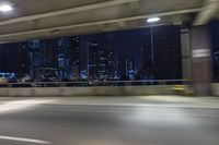 a car driving on the street at night with tall buildings in the background and two lights on and the vehicle is going through the intersection