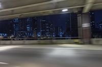 a car driving on the street at night with tall buildings in the background and two lights on and the vehicle is going through the intersection