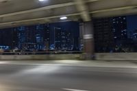 a car driving on the street at night with tall buildings in the background and two lights on and the vehicle is going through the intersection