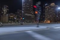 an empty city freeway at night with high rise buildings in the background with white and yellow lights