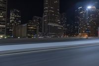 an empty city freeway at night with high rise buildings in the background with white and yellow lights