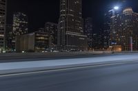 an empty city freeway at night with high rise buildings in the background with white and yellow lights