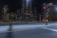 an empty city freeway at night with high rise buildings in the background with white and yellow lights