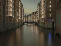 there are buildings along the water's edge at night, with lights reflecting off of the windows