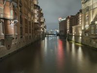 there are buildings along the water's edge at night, with lights reflecting off of the windows