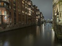 there are buildings along the water's edge at night, with lights reflecting off of the windows