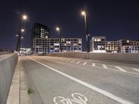 an empty roadway and light post with a few buildings in the background at night time