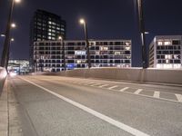 an empty roadway and light post with a few buildings in the background at night time