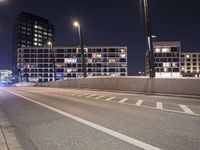 an empty roadway and light post with a few buildings in the background at night time