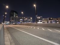 an empty roadway and light post with a few buildings in the background at night time