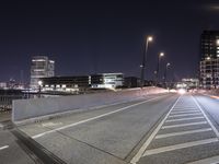 an empty roadway and light post with a few buildings in the background at night time