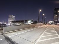 an empty roadway and light post with a few buildings in the background at night time