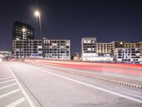 an empty roadway and light post with a few buildings in the background at night time