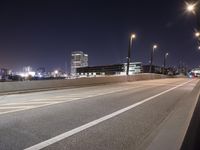 an empty roadway and light post with a few buildings in the background at night time