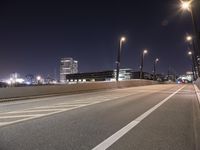an empty roadway and light post with a few buildings in the background at night time