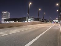 an empty roadway and light post with a few buildings in the background at night time
