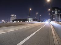 an empty roadway and light post with a few buildings in the background at night time