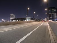 an empty roadway and light post with a few buildings in the background at night time