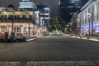 a city at night with an illuminated street and sidewalk area with benches and parked vehicles