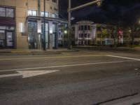 the traffic signal on the corner of the road is lit up at night time with a large building on the opposite side