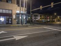 the traffic signal on the corner of the road is lit up at night time with a large building on the opposite side