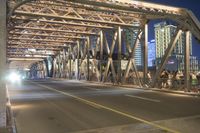 a long bridge spanning the street in front of a city at night, with several cars coming through it