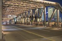 a long bridge spanning the street in front of a city at night, with several cars coming through it