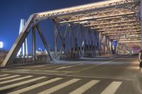 a long bridge spanning the street in front of a city at night, with several cars coming through it