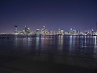 an ocean shore at night with city lights reflected in the water and piers below