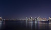 an ocean shore at night with city lights reflected in the water and piers below