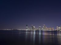 an ocean shore at night with city lights reflected in the water and piers below