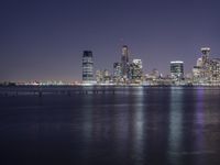 an ocean shore at night with city lights reflected in the water and piers below