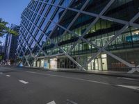 a city street at dusk near tall buildings with lights in the windows, the blue street lights are shining