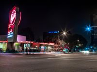 cars drive down the street near a large neon sign on a building at nighttime