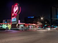 cars drive down the street near a large neon sign on a building at nighttime