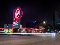 cars drive down the street near a large neon sign on a building at nighttime