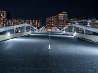 an empty street with white curved pedestrian crossing bridges at night time in the middle of a city