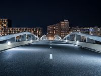 an empty street with white curved pedestrian crossing bridges at night time in the middle of a city