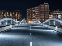 an empty street with white curved pedestrian crossing bridges at night time in the middle of a city