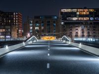 an empty street with white curved pedestrian crossing bridges at night time in the middle of a city