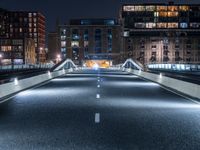 an empty street with white curved pedestrian crossing bridges at night time in the middle of a city