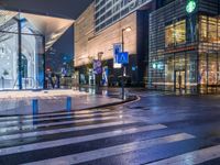 a view of a pedestrian crossing across from some other street lights at night time, with buildings in the background