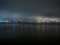 a city lit up on the waterfront at night with some lights reflecting in water and clouds