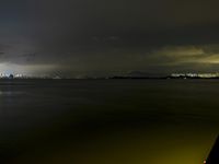 a city lit up on the waterfront at night with some lights reflecting in water and clouds