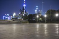 people walking along a plaza near a tall obelisk in the night, with an illuminated streetlight shining on it