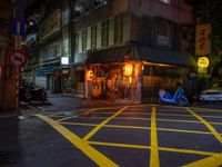 an empty street in the dark with traffic and shops on either side at night with yellow lighting