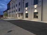 empty street next to some large building lit up at night - sized image with grey sky and a dark strip