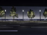 a large white building with trees on the street side at night time in front of it