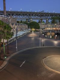 a wide road with an arched bridge in the background at night time - a few cars can be seen parked on the empty roadway