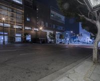 an empty street with a row of stores on one corner and the lights turned on at night